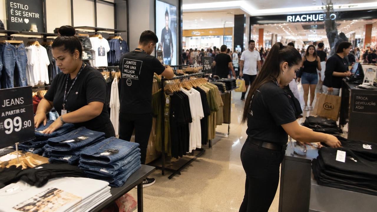 Vendedores organizando peças de roupa em uma loja de shopping movimentada no fim de semana