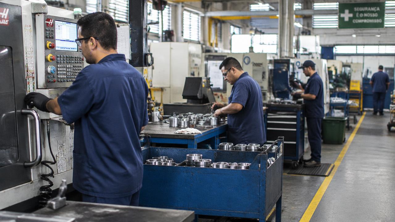 Operários trabalhando em máquinas no chão de fábrica de uma indústria